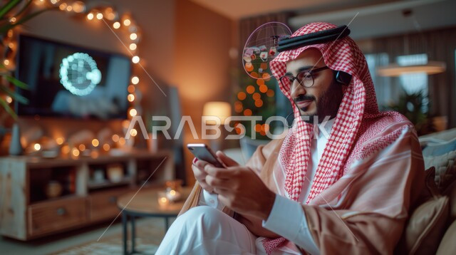 الاستماع إلى الموسيقا والتسجيلات الصوتية، استخدام الجوال والأجهزة التكنولوجية، رجل عربي خليجي سعودي يرتدي الزي التقليدي والبشت يجلس على كنبة مريحة داخل المنزل يقوم بتصفح تطبيقات الهاتف المحمول، الأثاث الراقي والديكورات الداخلية للشقق السكنية في السعودية