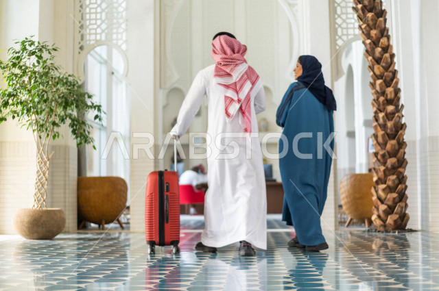 زوجان سعوديان سائحان في داخل الفندق السياحي لقضاء أجمل الأوقات , يمسك الزوج حقيبة السفر , سياحة وفندقة , قضاء أوقات عائلية ممتعة , سياحة وسفر