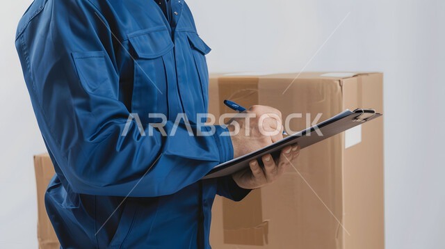 مفهوم التسوق الالكتروني, الطلبات الاونلاين والتسوق الذكي, عملية شحن وتوصيل موثوقه, بورتريه مقرب لرجل عربي خليجي سعودي يرتدي بدلة عمل زرقاء يعمل في توصيل الطلبات والبضائع للزبائن, كتابة وتسجيل البيانات والملاحظات، خلفية بيضاء