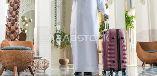 صورة مقربة لرجل أعمال خليجي سعودي يجر حقيبة سفر داخل الفندق , يرتدي ثوب أبيض , سياحة وفندقة , قضاء أوقات ممتعة