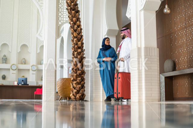 A Saudi couple smiling tourists inside the tourist hotel to spend the most beautiful times, the husband holds the travel bag, tourism and hotel management, spending enjoyable family times, tourism and travel