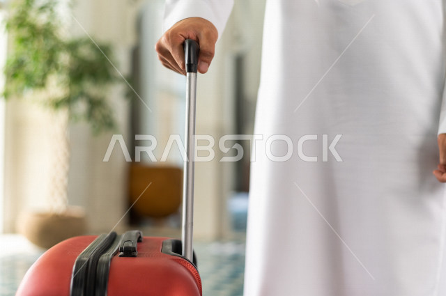 صورة مقربة لرجل أعمال خليجي سعودي يجر حقيبة سفر داخل الفندق , يرتدي ثوب أبيض , سياحة وفندقة , قضاء أوقات ممتعة