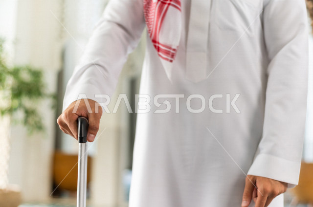 صورة مقربة لرجل أعمال خليجي سعودي يجر حقيبة سفر داخل الفندق , يرتدي ثوب أبيض , سياحة وفندقة , قضاء أوقات ممتعة