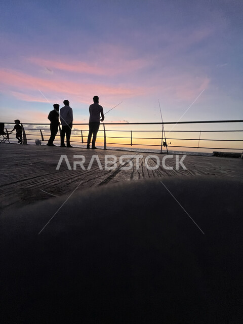 تأمل البحر وقت غروب الشمس، الكورنيش القديم المطل على البحر الأحمر، صورة ظلية لمجموعة من الشبان يتنزهون على ساحل مدينة جدة، أماكن سياحية في المملكة العربية السعودية، المناظر البحرية الهادئة، مفهوم صيد الأسماك، منظر الغيوم الوردية في السماء