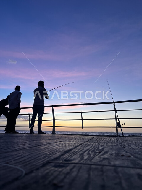 The old Corniche overlooking the Red Sea, silhouette of a group of young men walking on the coast of Jeddah, tourist places in the Kingdom of Saudi Arabia, peaceful seascapes, contemplating the sea at sunset, the concept of fishing, the view of pink clouds in the sky