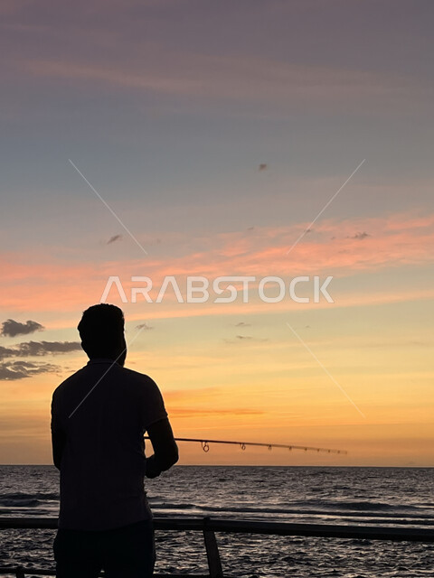 مفهوم صيد الأسماك، منظر الغيوم الوردية في السماء، الكورنيش القديم المطل على البحر الأحمر، صورة ظلية لشاب يقوم بالتنزه على ساحل مدينة جدة، أماكن سياحية في المملكة العربية السعودية، المناظر البحرية الهادئة، تأمل البحر وقت غروب الشمس