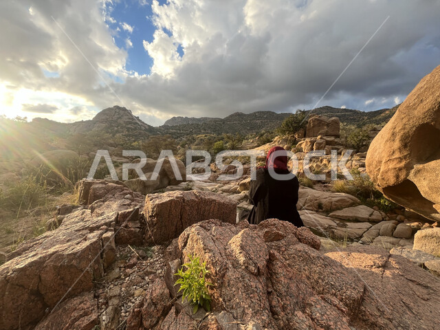 المناظر الطبيعية الهادئة، منظر الصخور والحجارة في الوديان، صورة من الخلف لشابة عربية خليجية سعودية تجلس في وادي الشفا في مدينة الطائف بالمملكة العربية السعودية، منظر الغيوم البيضاء في السماء، معالم أثرية سياحية، التضاريس والمرتفعات الجبلية