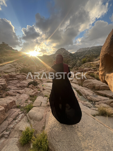 الاستمتاع بمشاهدة المناظر الطبيعية، منظر الصخور والحجارة في الوديان، صورة من الخلف لشابة عربية خليجية سعودية تسير في وادي الشفا في مدينة الطائف بالمملكة العربية السعودية، منظر الغيوم البيضاء في السماء، معالم أثرية سياحية، التضاريس والمرتفعات الجبلية