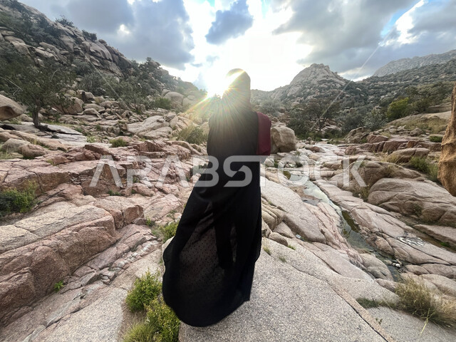 التشكيلات الطبيعية للصخور والحجارة في الوديان، صورة من الخلف لشابة عربية خليجية سعودية تسير في وادي الشفا في مدينة الطائف بالمملكة العربية السعودية، الأماكن الخصبة المليئة بالأشجار، منظر الغيوم البيضاء في السماء، معالم أثرية سياحية، التضاريس والمرتفعات الجبلية