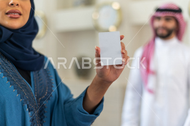 صورة مقربة لموظفة إستقبال خليجية سعودية محجبة تحمل كرت تعريفي فارغ بإيماءات وجه ويدين مختلفة , سياحة وفندقة , مكتب إستقبال العملاء , سياحة وسفر , خدمة العملاء في الفندق السياحي