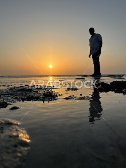 Sunset on Al Seef Beach, enjoying the scenery, silhouette of a young Saudi Arabian Gulf man standing on the coast of Jeddah city, concept of taking souvenir photos, calm sea nature