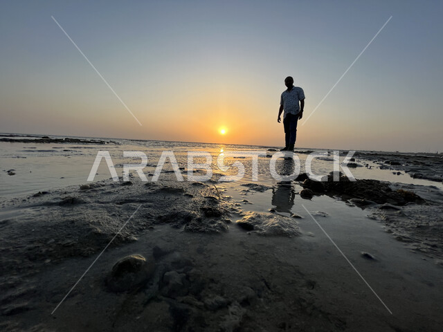 Sunset on Al Seef Beach, enjoying the scenery, silhouette of a young Saudi Arabian Gulf man standing on the coast of Jeddah city, concept of taking souvenir photos, calm sea nature