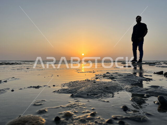 Enjoying the scenery, sunset on the Saif beach, concept of taking souvenir photos, calm sea nature, silhouette of a young Saudi Arabian Gulf man standing on the coast of the sea in Jeddah city