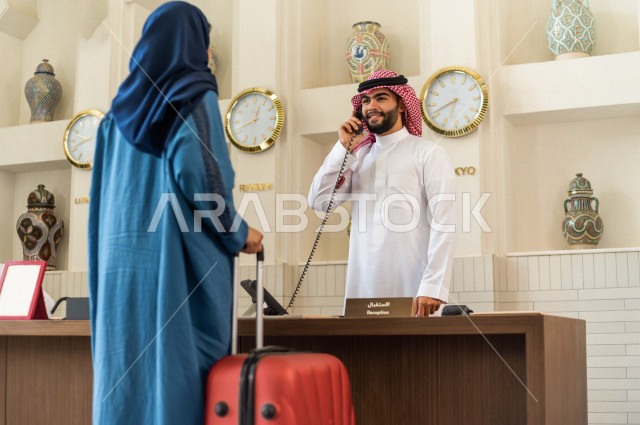 موظف إستقبال خليجي سعودي مبتسم يرحب بالنزيل السعودي ويتحدث على الهاتف في الفندق السياحي بإيماءات وجه ويدين مختلفة , سياحة وفندقة , خدمة ومكتب إستقبال العملاء , إجراءات الحجز والإستفسار , سياحة وسفر