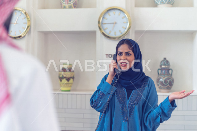 موظفة إستقبال خليجية سعودية محجبة مبتسمة ترحب بالنزيل السعودي وتتحدث على هاتف الفندق بإيماءات وجه ويدين مختلفة , سياحة وفندقة , خدمة ومكتب إستقبال العملاء , إجراءات الحجز والإستفسار , سياحة وسفر