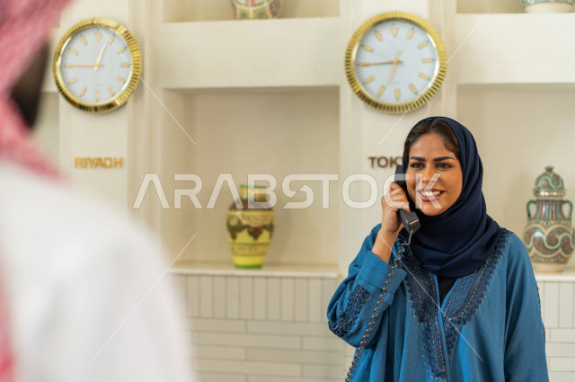 صورة مقربة لموظفة إستقبال خليجية سعودية محجبة مبتسمة تتحدث على الهاتف في الفندق السياحي بإيماءات وجه ويدين مختلفة , سياحة وفندقة , خدمة ومكتب إستقبال العملاء , إجراءات الحجز والإستفسار , سياحة وسفر