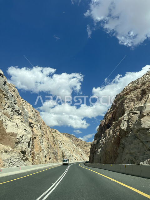 سيارة تسير في الممرات والطرقات المعبدة في مدينة الطائف، التضاريس والمرتفعات الجبلية، منظر الغيوم البيضاء في السماء، التكوينات والتشكيلات الطبيعية للصخور والحجارة، معالم وأماكن سياحية في السعودية، الطريق السريع لجبال الشفا