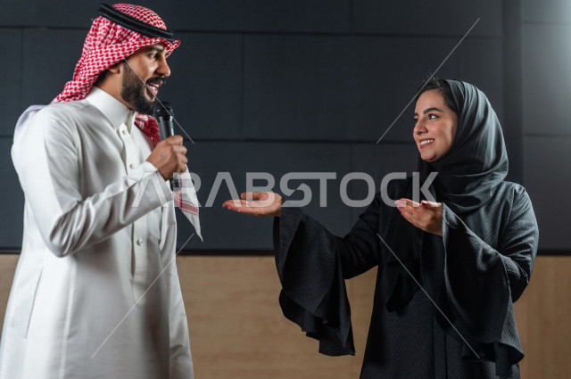 مرأه ورجل سعوديان خليجيان يقومان بالتقديم المسرحي على خشبة المسرح ، التفاعل مع الجمهور ، تحية الجماهير ،  تقديم العروضات المسرحية ، القاء الخطابات ، الحوارات و النقاشات ، اداء تمثيلي ، ايماءات وجه و يدين مختلفة ، الفن المسرحي