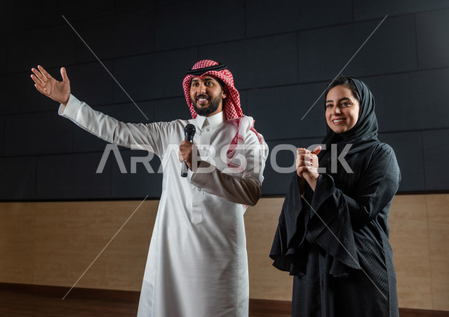 مرأه ورجل سعوديان خليجيان يقومان بالتقديم المسرحي على خشبة المسرح ، التفاعل مع الجمهور ، تحية الجماهير ،  تقديم العروضات المسرحية ، القاء الخطابات ، الحوارات و النقاشات ، اداء تمثيلي ، ايماءات وجه و يدين مختلفة ، الفن المسرحي