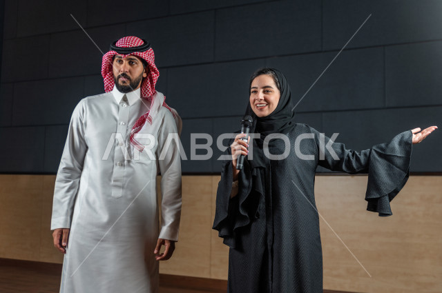 مرأه ورجل سعوديان خليجيان يقومان بالتقديم المسرحي على خشبة المسرح ، التفاعل مع الجمهور ، تحية الجماهير ،  تقديم العروضات المسرحية ، القاء الخطابات ، الحوارات و النقاشات ، اداء تمثيلي ، ايماءات وجه و يدين مختلفة ، الفن المسرحي