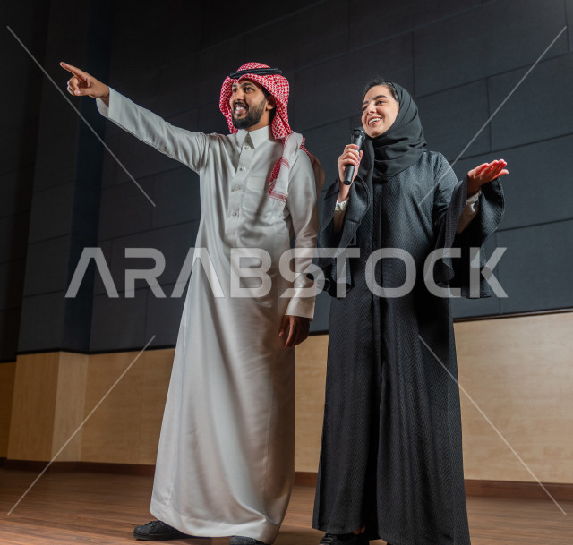 مرأه ورجل سعوديان خليجيان يقومان بالتقديم المسرحي على خشبة المسرح ، التفاعل مع الجمهور ، تحية الجماهير ،  تقديم العروضات المسرحية ، القاء الخطابات ، الحوارات و النقاشات ، اداء تمثيلي ، ايماءات وجه و يدين مختلفة ، الفن المسرحي