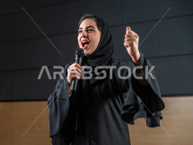 مرأه سعودية خليجية تقوم بالتقديم المسرحي على خشبة المسرح تتفاعل مع الجمهور ،  تقديم العروضات المسرحية ، القاء الخطابات ، الحوارات و النقاشات ، اداء تمثيلي ، ايماءات وجه و يدين مختلفة ، الفن المسرحي