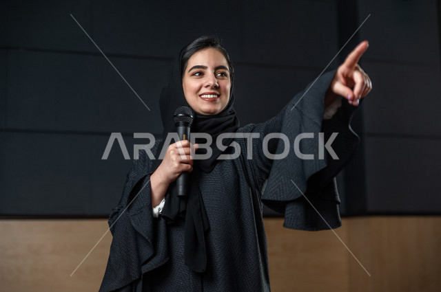 مرأه سعودية خليجية تقوم بالتقديم المسرحي على خشبة المسرح تتفاعل مع الجمهور ،  تقديم العروضات المسرحية ، القاء الخطابات ، الحوارات و النقاشات ، اداء تمثيلي ، ايماءات وجه و يدين مختلفة ، الفن المسرحي