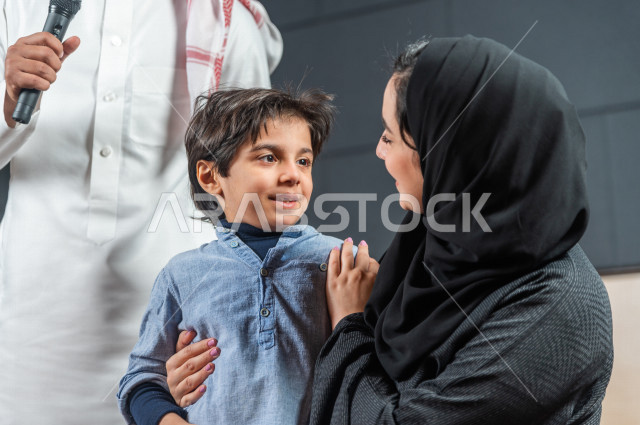 A Saudi Gulf boy in one of the theatrical parties, standing on the stage with his parents, encouraging the parents for the children, honoring the outstanding student in front of the audience in the school theater, an acting performance, greeting the masse