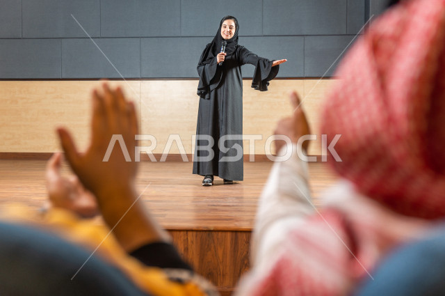 مرأه سعودية خليجية تقوم بالتقديم المسرحي على خشبة المسرح ، تتفاعل مع الجمهور ، تحية الجماهير ،  تقديم العروضات المسرحية ، القاء الخطابات ، الحوارات و النقاشات ، اداء تمثيلي ، ايماءات وجه و يدين مختلفة ، الفن المسرحي 