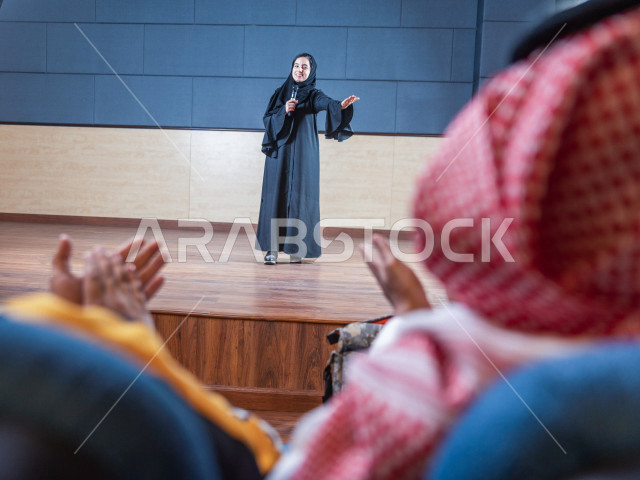 مرأه سعودية خليجية تقوم بالتقديم المسرحي على خشبة المسرح ، تتفاعل مع الجمهور ، تحية الجماهير ،  تقديم العروضات المسرحية ، القاء الخطابات ، الحوارات و النقاشات ، اداء تمثيلي ، ايماءات وجه و يدين مختلفة ، الفن المسرحي 