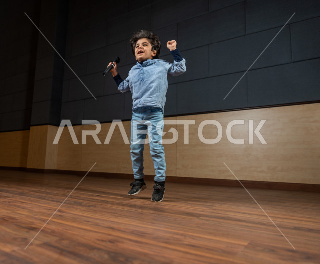 فتى سعودي خليجي في احدى الحفلات المسرحية ، يقفز فرحا على خشبة المسرح ، تكريم  الطالب المتفوق أمام الحضور في المسرح المدرسي  ، تعابير و ايماءات وجه و يدين تدل على الفرحة و السعادة  ، اداء تمثيلي