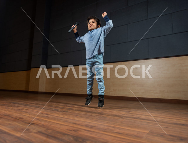 A Saudi Gulf boy in one of the theatrical parties, jumping for joy on the stage, honoring the outstanding student in front of the audience in the school theater, expressions and gestures of the face and hands indicating joy and happiness, an acting perfor