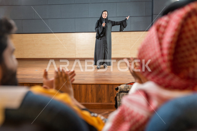 مرأه سعودية خليجية تقوم بالتقديم المسرحي على خشبة المسرح ، تتفاعل مع الجمهور ، تحية الجماهير ،  تقديم العروضات المسرحية ، القاء الخطابات ، الحوارات و النقاشات ، اداء تمثيلي ، ايماءات وجه و يدين مختلفة ، الفن المسرحي 
