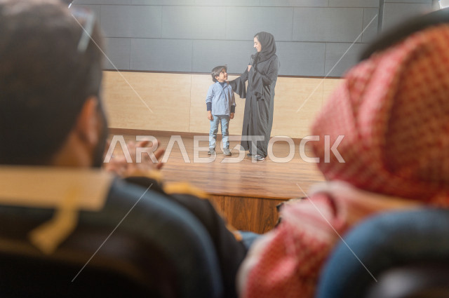 لقطة تصوير معلمة سعودية تكرم طالب أمام الحضور في المسرح المدرسي ,  طفل خليجي صغير يتحدث وبيده المايكرفون , مسرح تعليمي  
