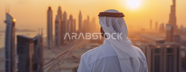 Consider the tourist places in the United Arab Emirates, the progress and development of architectural art, landmarks and architectural facilities at sunset, a picture from behind of an Arab Gulf Emirati man wearing the traditional dress and white ghutra, standing upright in front of the skyscrapers and towers in the city of Dubai.