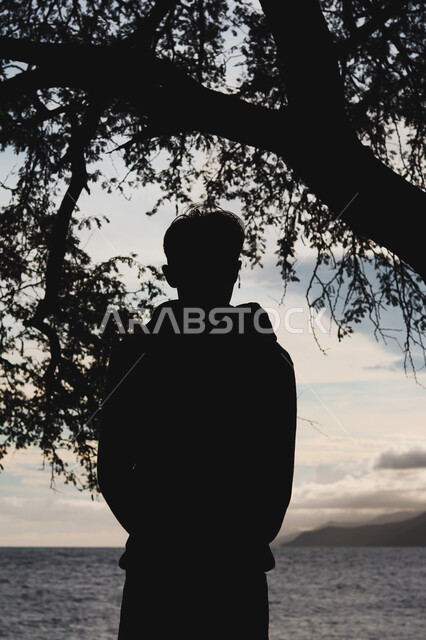  قضاء وقت ممتع بتأمل مناظر الطبيعة الهادئة، صورة ظلية من الخلف لشاب عربي خليجي سعودي يقف على الشاطئ الرملي، الاستمتاع بالنظر الى ساحل البحر، الواجهة البحرية والمناطق الطبيعية في المملكة العربية السعودية، النزهات والرحلات في فصل الصيف، سالوييت