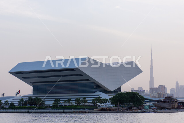 منارة ثقافية مشهورة في الامارات العربية المتحدة, تصميم المكتبة الفريد على شكل كتاب مفتوح, مراكز نشر الكتب والمطبوعات, خلفية ضبابية ببرج خليفة الشامخ، الموقع المتميز على ضفاف خور دبي لمكتبة محمد بن راشد آل مكتوم