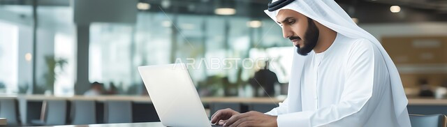مهن ووظائف ادارية مكتبية, دمج التكنولوجيا مع الحياة العملية، إدارة شؤون الأعمال وتنظيمها عبر الاجهزة التقنية، صورة بانورامية لرجل اعمال عربي خليجي سعودي يرتدي الزي التقليدي يقوم بالعمل على الحاسوب المحمول داخل المكتب