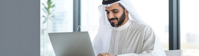 إدارة شؤون الأعمال وتنظيمها عبر الاجهزة التقنية، دمج التكنولوجيا مع الحياة العملية، مهن ووظائف ادارية مكتبية, صورة بانورامية لرجل اعمال عربي خليجي سعودي يرتدي الزي التقليدي يقوم بالعمل على الحاسوب المحمول داخل المكتب