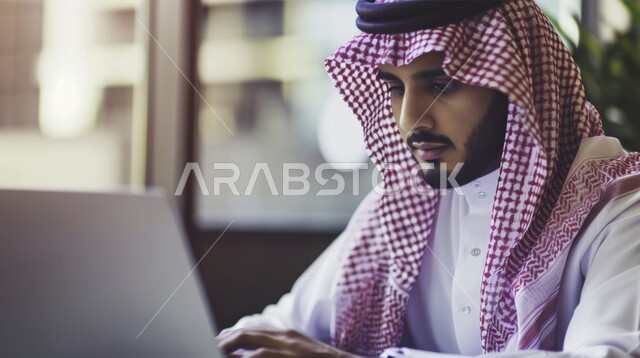 إدارة شؤون الأعمال وتنظيمها عبر الاجهزة التقنية، دمج التكنولوجيا مع الحياة العملية، مهن ووظائف ادارية مكتبية, صورة مقربة لرجل اعمال عربي خليجي سعودي يرتدي الزي التقليدي يقوم بالعمل على الحاسوب المحمول داخل المكتب، إيماءات الاندماج والتركيز