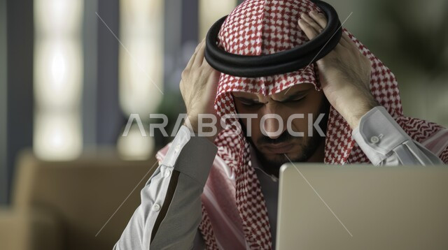 مهن ووظائف مكتبية, إيماءات الصداع والضجر, صورة مقربة لرجل عربي خليجي سعودي يرتدي الشماغ والثوب التقليدي يضع يديه على رأسه يقوم باستخدام الحاسب المحمول, مفهوم ضغط العمل, تعابير الحزن والتعب, إدارة وتنظيم الأعمال ضمن مقر الشركة
