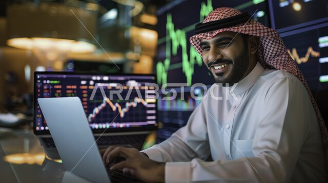 إدارة الأعمال عن بعد, صورة مقربة من الجانب لرجل عربي خليجي سعودي يرتدي الشماغ والثوب التقليدي يقوم بانجاز المهام عبر الحاسب المحمول, استخدام الأجهزة والتقنيات الحديثة, الاقتصاد والأمور المالية, خلفية شاشة رقمية لأسهم البورصة