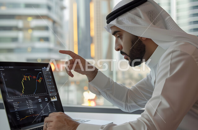 إدارة شؤون الأعمال وتنظيمها عبر الاجهزة التقنية، دمج العمل مع التكنولوجيا، مهن ووظائف مكتبية،رجل اعمال عربي خليجي سعودي يرتدي الزي التقليدي والغترة يعمل على الحاسوب المحمول, العمل في المجال الاقتصادي, عرض المخططات البيانية المالية