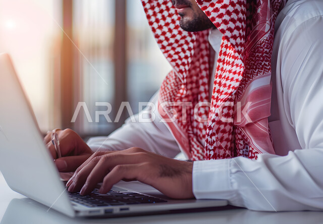 وظائف ومهن مكتبية سعودية، دمج العمل مع التكنولوجيا، العمل في المجال الاقتصادي, إنجاز المهام المطلوبة، إدارة شؤون الشركة وتنظيمها عبر الاجهزة التقنية، صورة مقربة لرجل عربي خليجي سعودي يرتدي الزي التقليدي والشماغ يعمل على الحاسوب المحمول