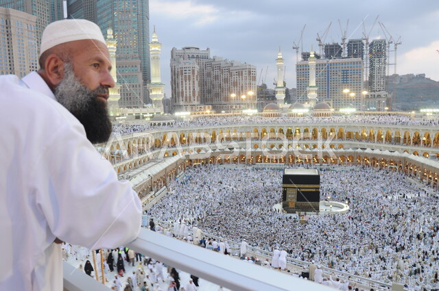 Circumambulating around the Holy Kaaba in Mecca, gathering of pilgrims and Umrah pilgrims in the courtyard of the Grand Mosque, performing Hajj and Umrah rituals, the Holy Mosque of Mecca in the Kingdom of Saudi Arabia, sacred Islamic religious monuments and places, worship and getting closer to God Almighty, a close-up picture of a man standing in front of the Holy Kaaba during the day.