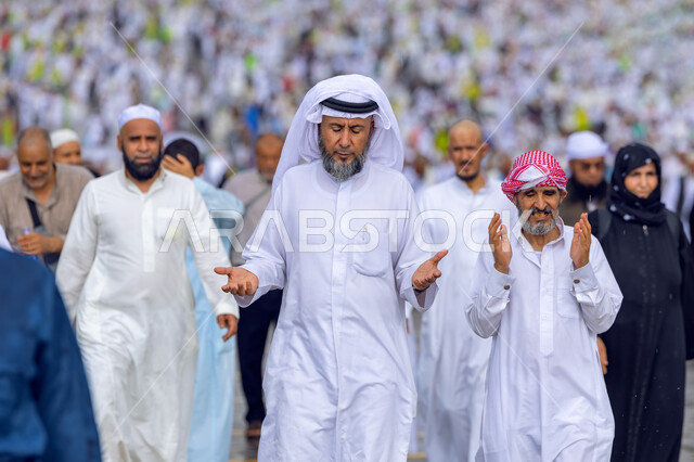 أداء مناسك الحج و العمرة , العبادة و التقرب إلى الله , زيارة بيت الله الحرام في مكة المكرمة , مجموعة من المسلمين العربيين يرتدون الزي التقليدي يرفعون أيديهم بتعابير الدعاء , الركن الخامس من أركان الإسلام