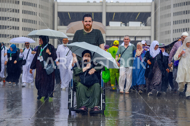 Worship and getting closer to God, visiting the Sacred House of God in Mecca, a young Muslim man helping his mother with special needs perform Hajj and Umrah rituals, the fifth pillar of Islam, the concept of honoring one’s parents, a rainy winter atmosphere in the Kingdom of Saudi Arabia