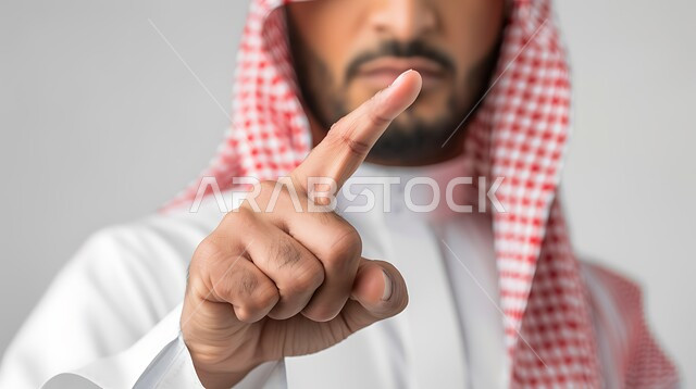 الاشارة إلى شيء ما بإيماءات التحديد والتأكيد, بورتريه لرجل عربي خليجي سعودي يرتدي الزي التقليدي والشماغ يشير بأصابع السبابة بتعابير التحذير والتنبيه، خلفية رمادية