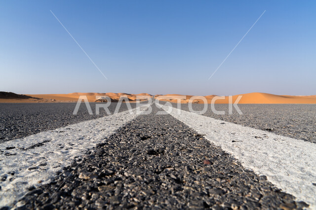 النمو والتطور العمراني في صحاري المملكة, البيئة الصحراوية الجافة في السعودية, صورة مقربة لطريق اسفلتي ممتد على طول الصحراء, خطا المرور الأبيضان لزيادة الأمان, شارع معبد للسيارات وتسريع حركة المسافرين, تسهيل التنقلات بين المناطق البرية والمدن