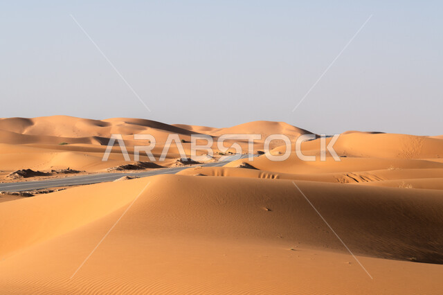 البيئة الصحراوية الجافة في السعودية, طريق اسفلتي ممتد على طول الصحراء, تشكل الكثبان والتلال الرملية, النمو والتطور العمراني في صحاري المملكة, شارع معبد لمرور السيارات وتسريع حركة المسافرين, تسهيل التنقلات بين المناطق البرية والمدن